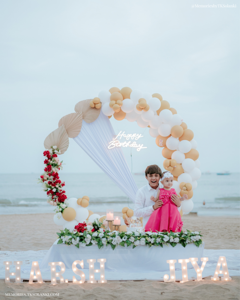 Beach birthday setup in Diu with white and gold balloons, flowers and birthday cake